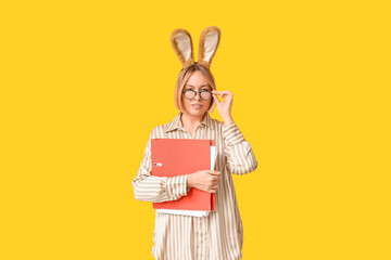 Wall Mural - Adult female secretary in bunny ears with documents folder on yellow background. Easter celebration