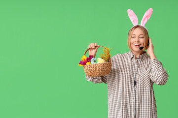 Wall Mural - Happy adult female operator in bunny ears with headset and basket for Easter on green background