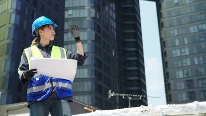 Wall Mural - Professional Asian woman engineer in safety uniform working with blueprint at outdoor construction site building rooftop. Architecture technician inspector inspect building exterior structure system.