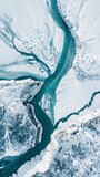 Fototapeta Tęcza - Aerial view of a frozen river winding through a snowy landscape