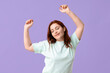 Beautiful young redhead woman dancing on lilac background