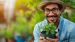 A cheerful man with glasses and a fedora hat tenderly holds a potted young plant