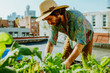 man in a boho shirt and straw hat tending to his rooftop garden
