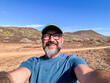 © simona - Cheerful happy adult man taking selfie picture smiling and enjoying outdoor leisure activity with desert and mountains in background. Scenic travel location for male traveler