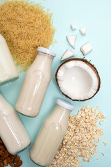 Wall Mural - Types of plant-based milk in glass bottles. Coconut, rice, almond and oat milk on blue background.