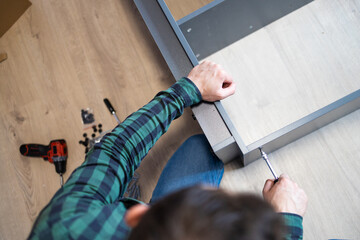 Furniture assembly. The furniture assembler takes a white shelf, tightens the screw with a hex wrench. Collector of furniture. Moving concept, furniture assembler, self assembly