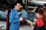 Fototapeta Dziecięca - Asian male professional automotive engineer supervisor describes car wheel and suspension repair work with mechanic worker staffs team in fix service garage, specialist occupations in auto industry.