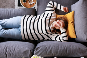 Lonely young woman lying on her back on comfortable sofa at home