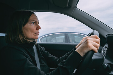 Caucasian female hands holding car steering wheel while driving through countryside landscape