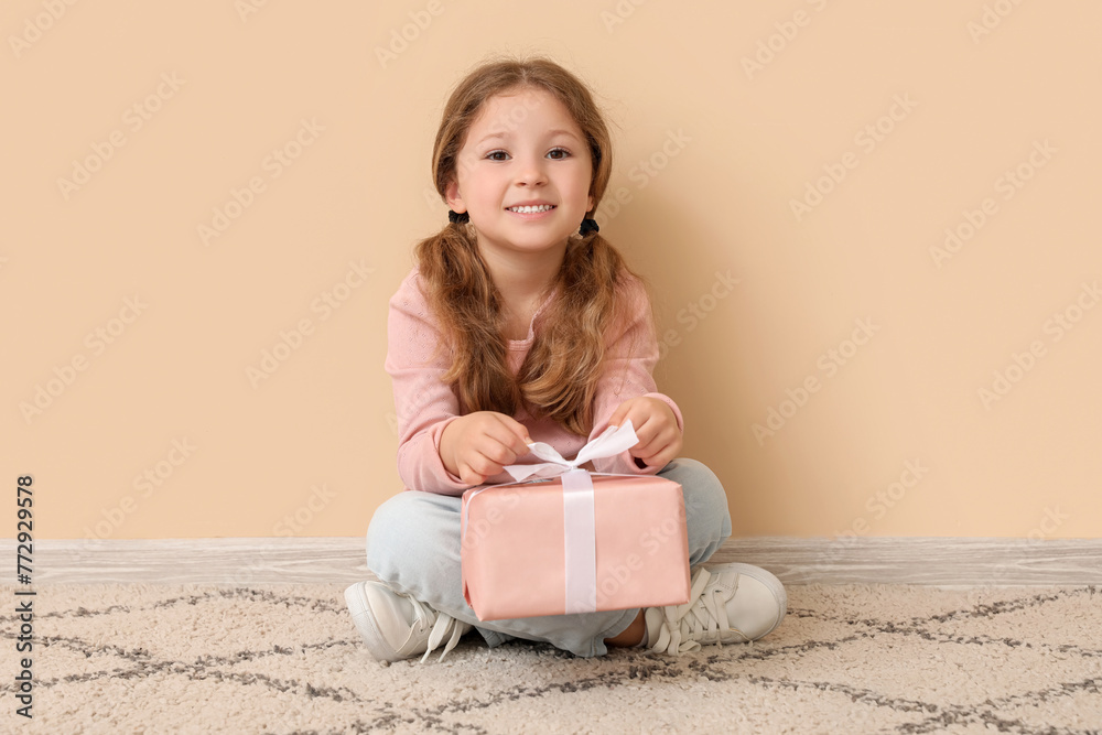 Little girl with gift sitting near beige wall. Children's Day celebration