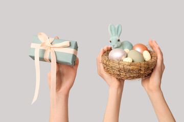 Female hands holding nest with Easter eggs, bunny and gift box on white background