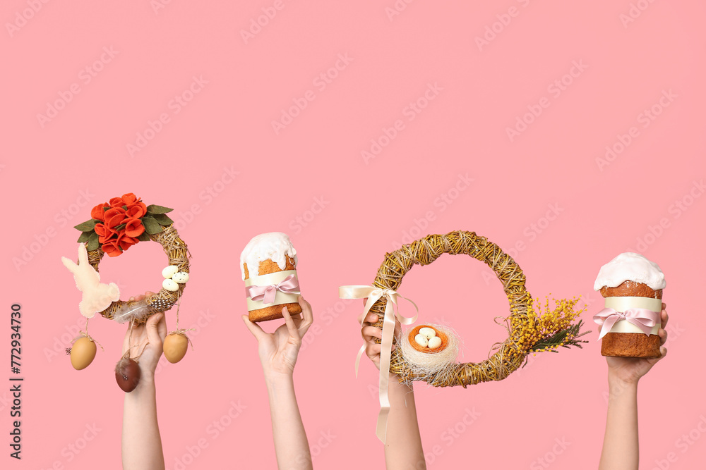 Female hands with Easter cakes and festive wreaths on pink background