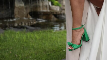 Sticker - leg of the bride in a white wedding dress and green shoes in the park