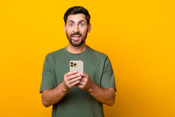 Wall Mural - Photo portrait of handsome young guy hold telephone excited dressed stylish khaki outfit isolated on yellow color background