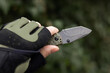 Hand in tactical glove, holding folding knife,