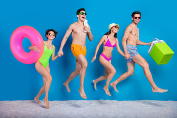 Wall Mural - Full length photo of excited funky fellows company wear swimsuits jumping high running beach party isolated blue color background