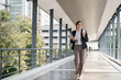 Young busy successful Asian business woman, professional businesswoman holding laptop and holding coffee cup standing or walking on urban business center