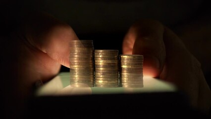 Poster - Columns of coins grow against the background of hands using a smartphone in the dark. Cg
