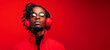 A afro american man wearing red glasses and headphones is standing in front of a red background. Concept of relaxation and enjoyment, as the man is likely listening to music or an audio recording.