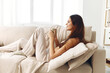 © SHOTPRIME STUDIO - Cozy Morning Bliss: Smiling Woman Holding a Coffee Mug, Wrapped in a Blanket, Relaxing on a Warm Autumn Weekend in Her Comfortable Home
