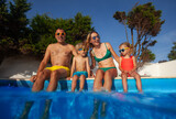 Fototapeta  - Two adults with kids having fun at pool party in summer resort