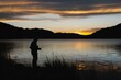 silhouette of a person fly fishing against a mountain lake sunset