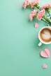 Mother's Day magic: Overhead vertical view of pink carnations, cup of coffee with heart-shaped foam, and paper hearts on teal background with space for messages