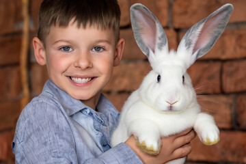 Wall Mural - boy with a rabbit. a small cheerful boy in a light shirt stands against the background of a brick wall with a fluffy rabbit in his hands, animal concept