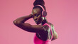 Fitness woman showing muscles wearing pink sportswear with headphones on a coral background. Studio health and wellness concept for design and print. Portrait orientation with copy space