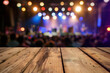 Empty wooden table top with blurred concert stage and crowd in the background, for product display presentation or montage of your products. Blurred night scene with bokeh lights, copy space.