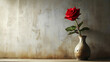 A single red rose flower in a ceramic vase standing on a textured beige wall background with empty copy space. Elegant home decor