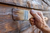 Fototapeta  - Close-up of a hand applying brown paint on wooden planks with a brush.