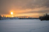 Fototapeta Natura - Scenic winter landscape featuring a vast, snow-blanketed field with trees at sunset