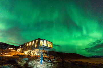 Wall Mural - aurora borealis, northern lights glowing over luxury hotel and male tourist enjoying on mount hengil