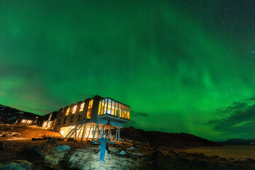 Wall Mural - aurora borealis, northern lights glowing over luxury hotel and male tourist enjoying on mount hengil