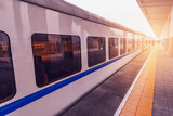 Fototapeta Koty - Passenger train stands by the platform at sunset.
