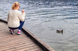 © astrosystem - Woman feeding ducks on a lake.