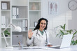 Cheerful Hispanic female doctor waving hand in greeting at her office, representing approachable healthcare professionals.