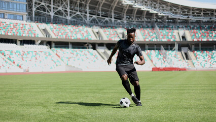 African American man playing football on the stadium field. A man runs with a soccer ball across the field.