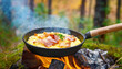 Scrambled eggs with bacon cooking in a cast iron pan, on an open fire.