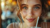 Fototapeta  - Close-up shot capturing her with a straw in her mouth and a cup in front of her face, straw poking out. Reflect the joy of a refreshing moment
