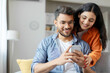 © Home-stock - Cheerful indian couple using cellphone, shopping online, spouses sitting on sofa at home interior