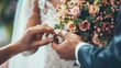 Close-up of a couple exchanging wedding rings, with a bouquet of flowers in the background