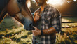 A closeup of a man wearing a rugged flannel shirt, standing beside a calm horse in a sunlit pasture. The man is gently holding the horses bridle, showing a connection of trust and friendship