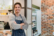 Smiling young white handsome barista standing with his arms crossed in coffee shop. Caucasian male bartender shop assistant vendor waiter looking at camera in cafeteria restaurant