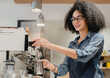 20s afro female barista making coffee using coffee machine in cafeteria, brewing drip filter from quality beans in restaurant behind the bar counter in restaurant