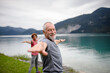 Senior couple doing outdoor yoga, tai chi, pilates by the lake in the autumn. Elderly husband and wife spending active vacation in the mountains. Pensioners stretching after outdoor workout