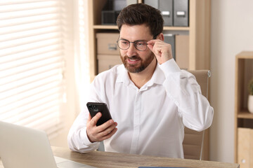 Canvas Print - Smiling man using smartphone at table in office