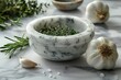 White marble mortar and pestle with thyme, rosemary and garlic on a grey background