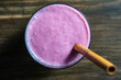Raspberry banana smoothie with a bamboo straw on a wooden table, closeup, top view